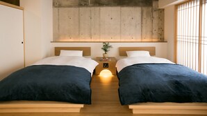 A modern bedroom with two beds, a concrete ceiling, wooden headboards, and a bedside table with a plant.