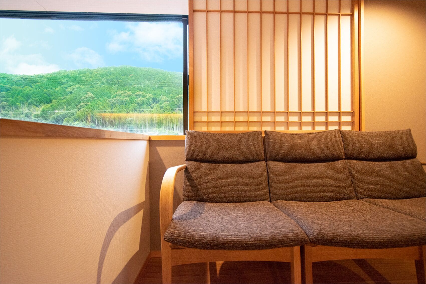 A room with a view of a green landscape through a window, a wooden chair, and a shoji screen.