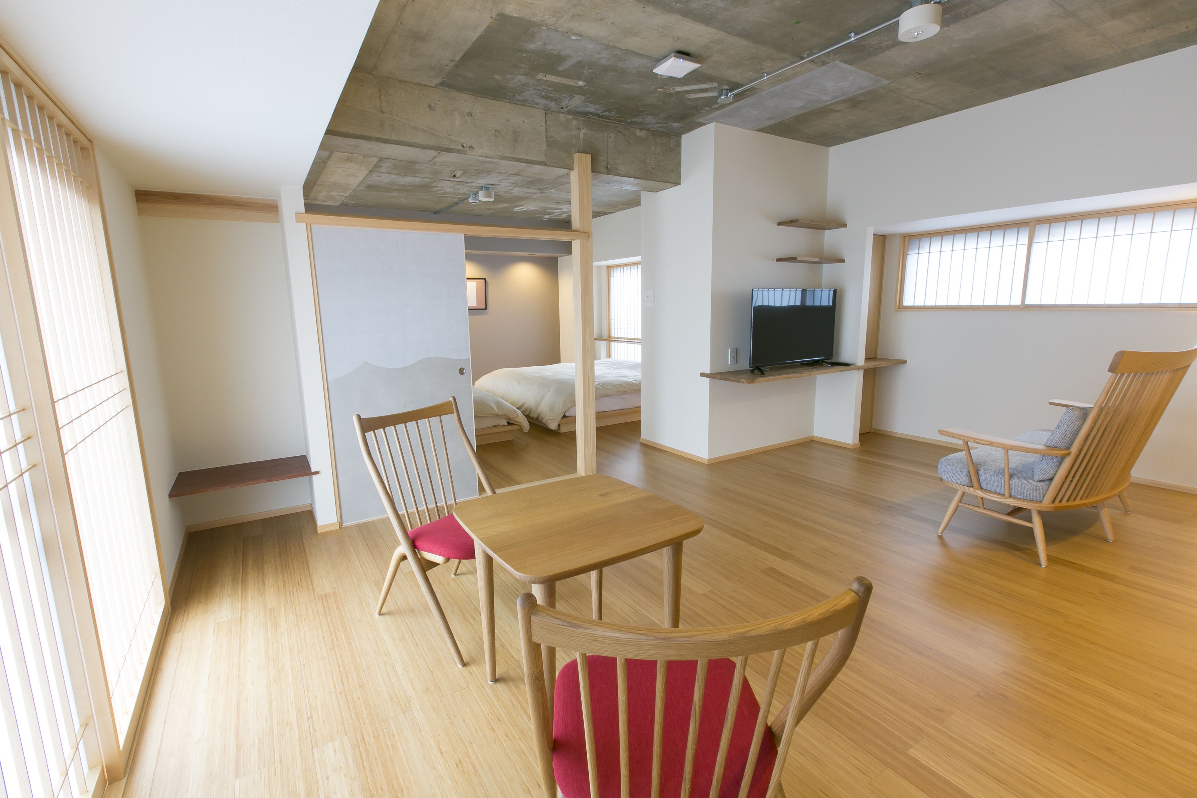 Un espace de vie moderne, à aire ouverte, avec un plancher en bois, une table à manger, deux chaises, un téléviseur posé sur une étagère et un lit à l’arrière-plan.