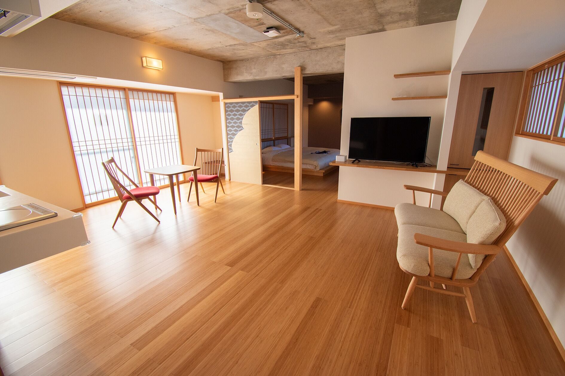 A modern living room with wooden flooring, a TV, a sofa, and a dining area with chairs.