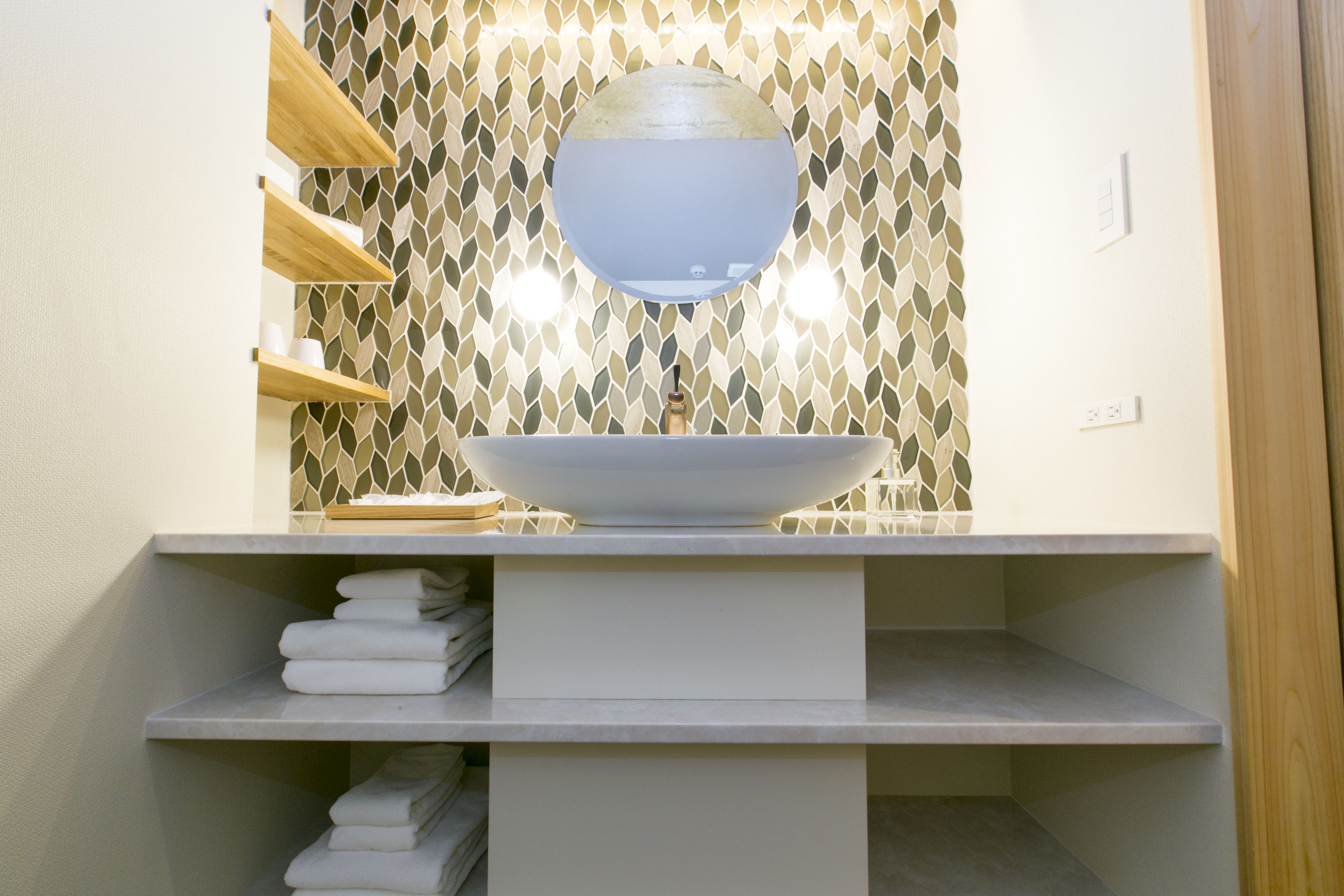 Une salle de bain avec un lavabo blanc, un miroir rond et un mur orné d’un motif.