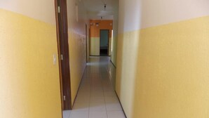 A narrow hallway with yellow walls and a tiled floor, leading to a room with an orange wall. - Pousada Cariri (Juazeiro do Norte)