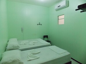 Une petite chambre d’hôtel composée d’une seule pièce, avec deux lits, une petite fenêtre, un appareil de climatisation et une chaise.