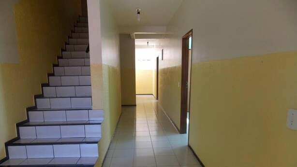 A hallway with a staircase leading to an upper floor, tiled floors, and yellow walls. - Pousada Cariri (Juazeiro do Norte)
