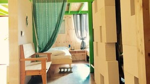 A room with a bed, a chair, a small table, and a green curtain. - Family Hotel Oliva (Jeju City)