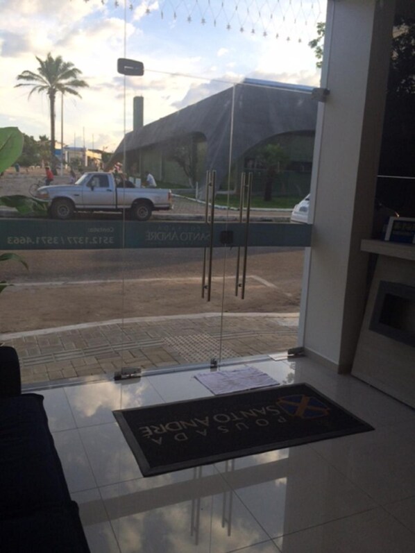 A hotel reception area with a clear view of the street outside, including a parked white car and a building with a large awning. - Pousada Santo Andre - O Apostolo (Juazeiro do Norte)