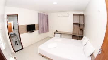 Una habitación de hotel con cama, televisor, armario y espejo.