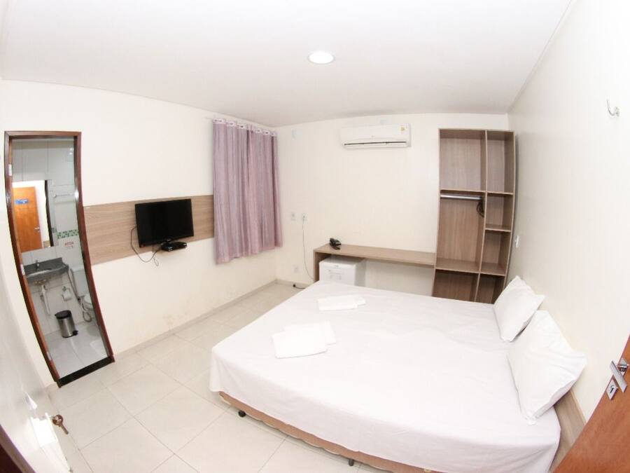 Una habitación de hotel con cama, televisor, armario y espejo.