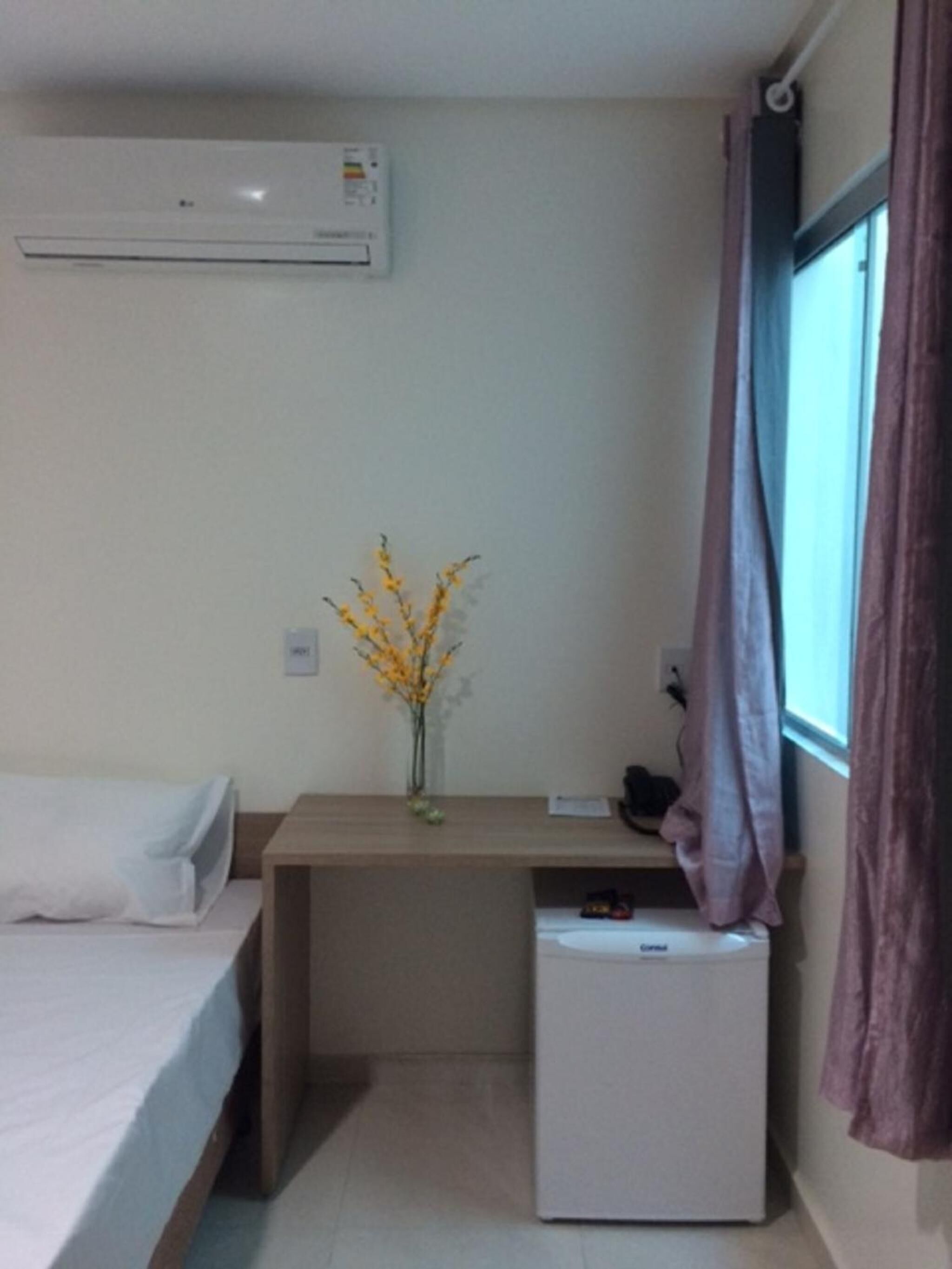 Habitación de hotel con cama, escritorio, un refrigerador pequeño y ventana con cortinas.