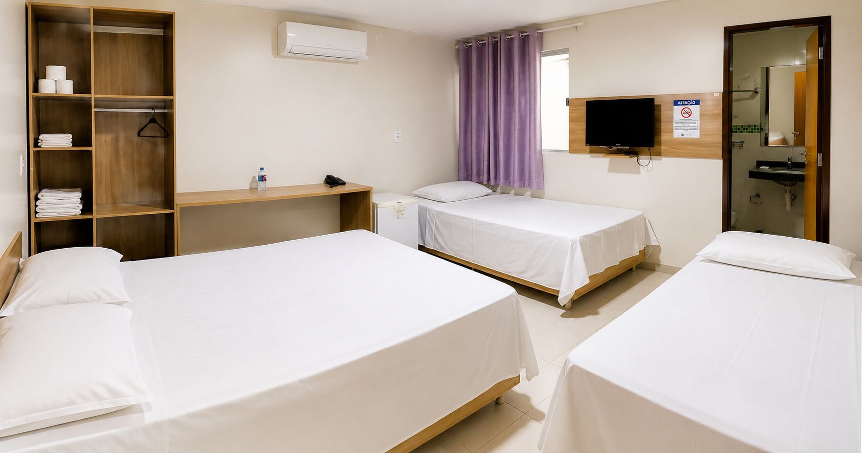 A hotel room with two beds, a wardrobe, a desk, a television, and a bathroom visible through an open door.