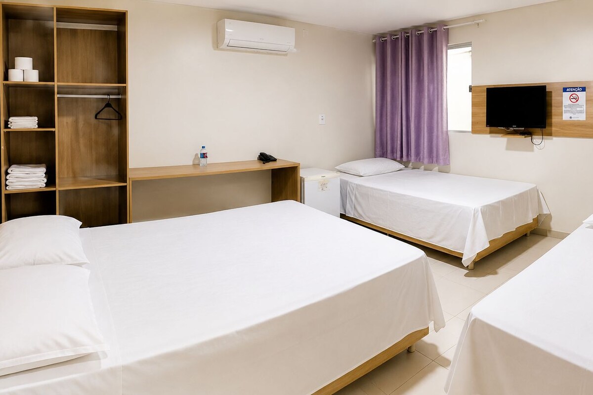 Ein Hotelzimmer mit zwei Betten, einem Kleiderschrank, einem Schreibtisch, einem Fernseher und einem durchgegangenen Badezimmer.