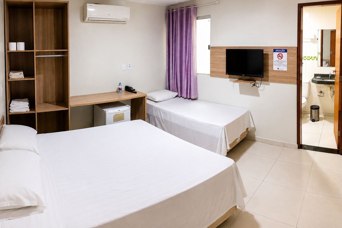 Ein Hotelzimmer mit zwei Betten, einem Schreibtisch, einem Fernseher und einem durch eine offene Tür einsehbarer Badezimmer.