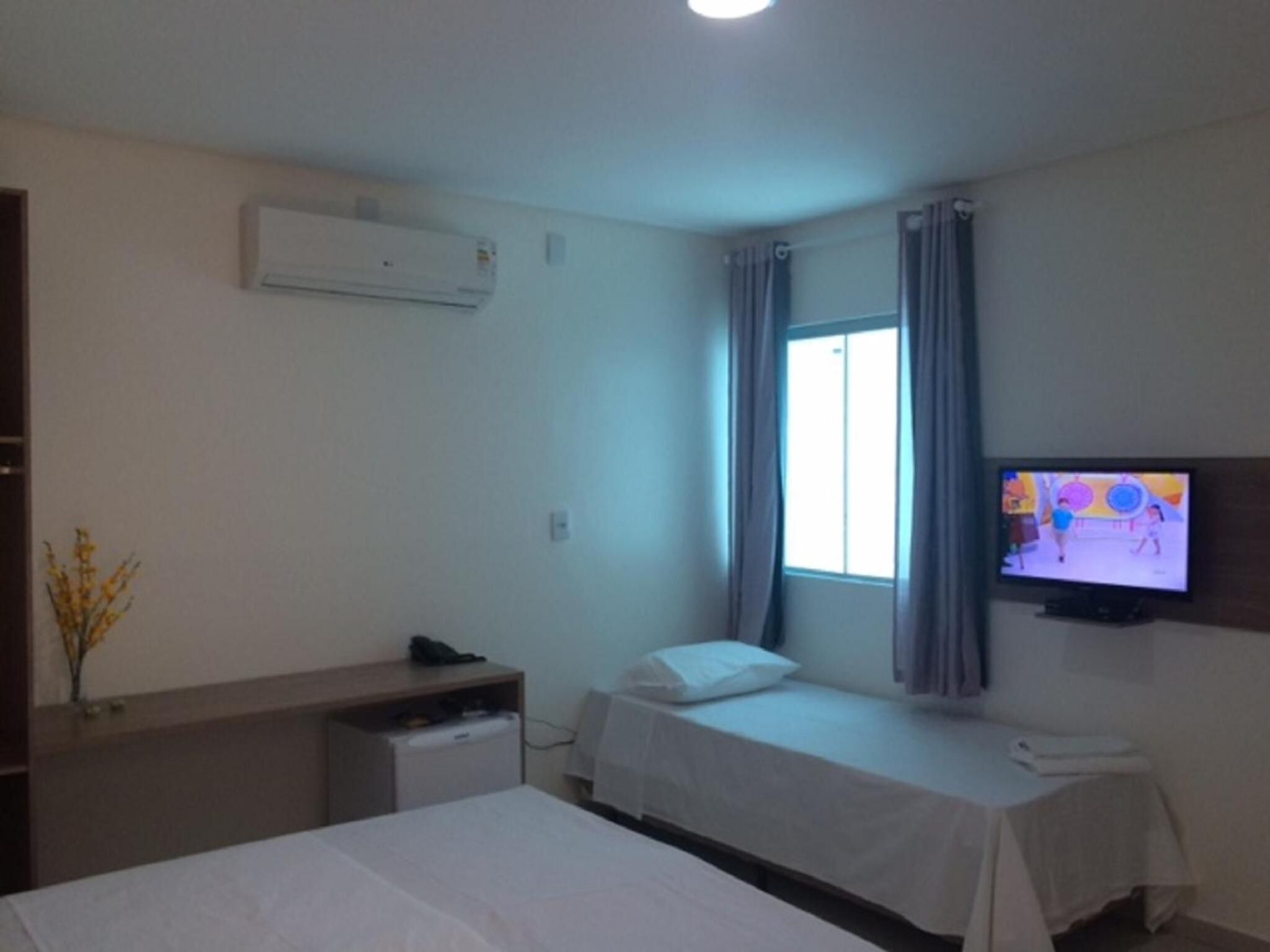 Habitación de hotel con dos camas, un escritorio, un televisor y una ventana con cortinas.