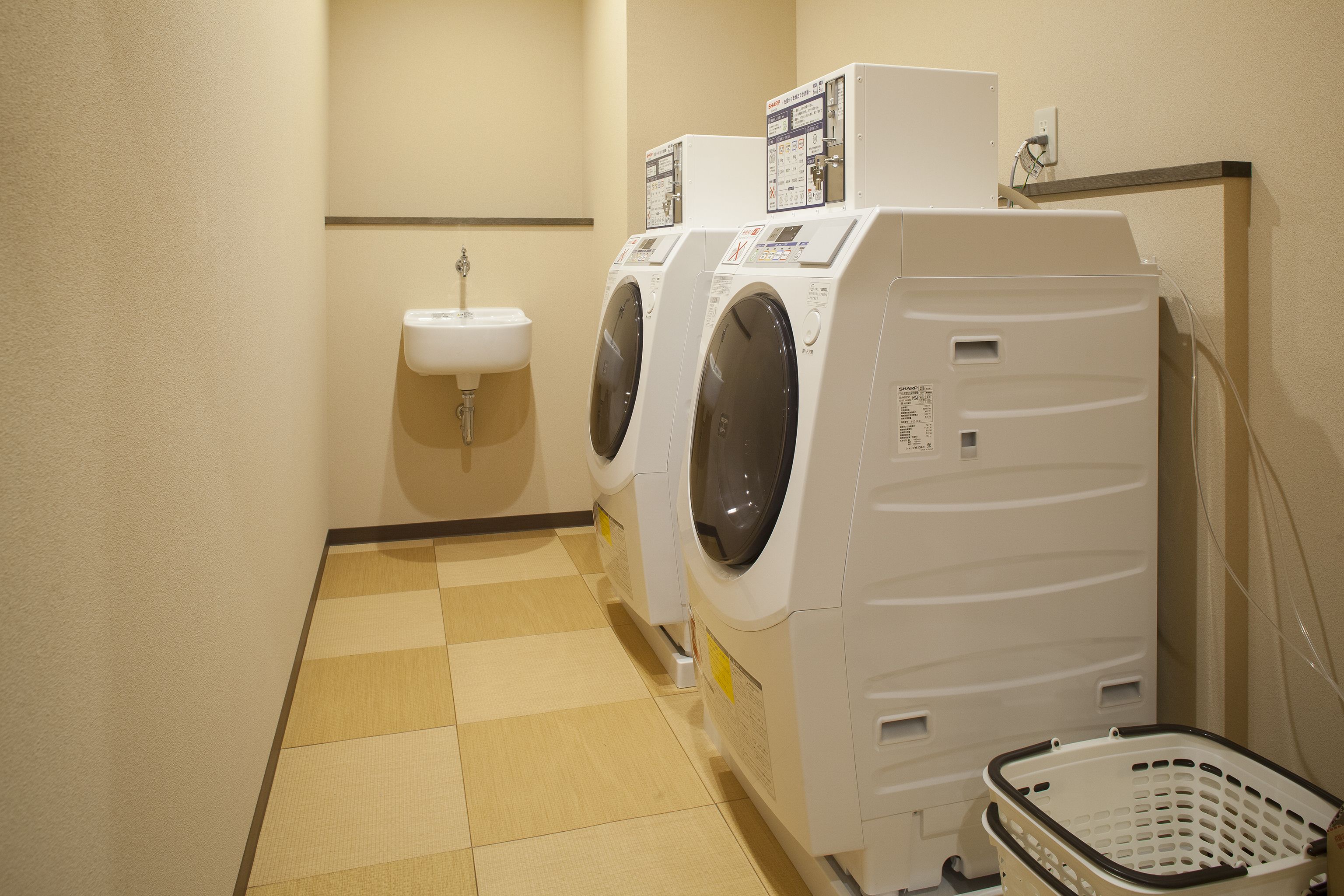 A laundry room with two front-loading washing machines, a sink, and a basket.