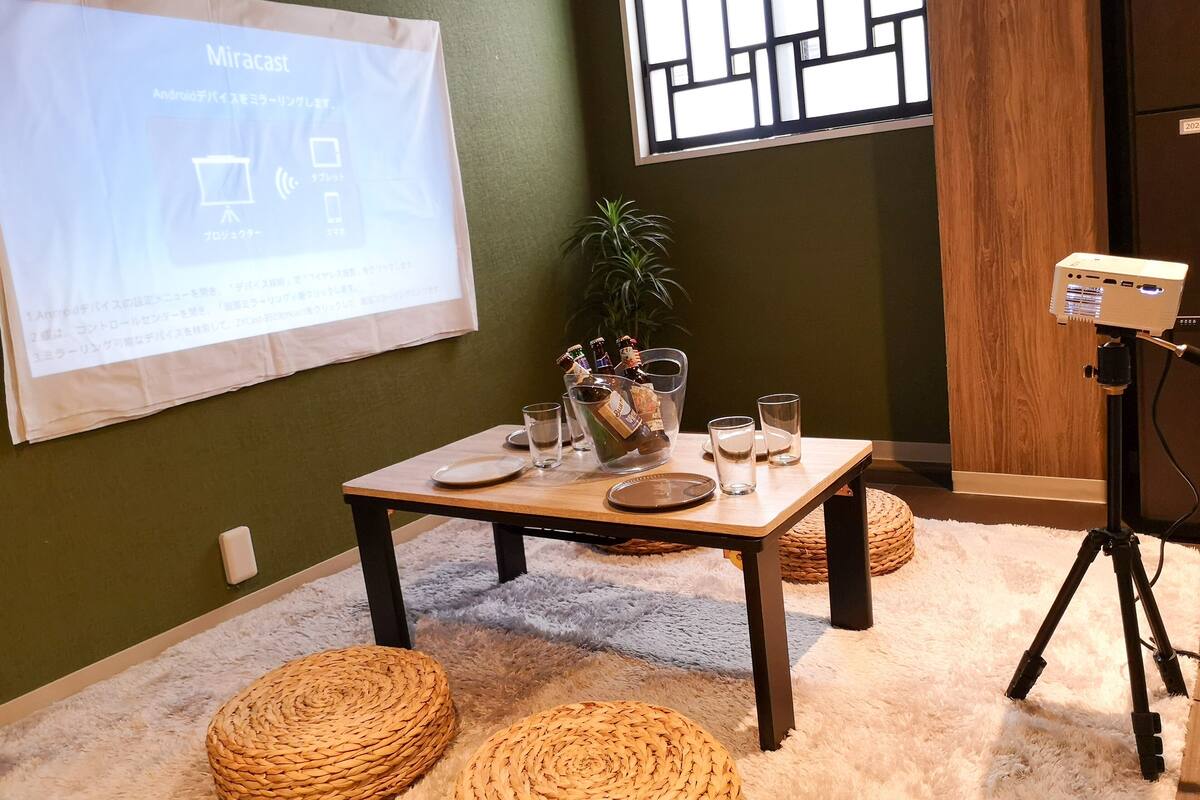 A room with a projector screen displaying a presentation, a table with glasses and bottles, and a tripod with a camera.