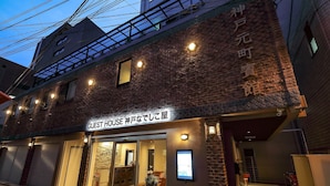 A hotel with a brick facade, a sign reading "GUEST HOUSE," and a visible entrance with a glass door. - Guest House Kobe Nadeshikoya - Hostel (Kobe)