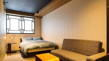 Un dormitorio con cama, sofá, una mesita y un ventanal de diseño geométrico.