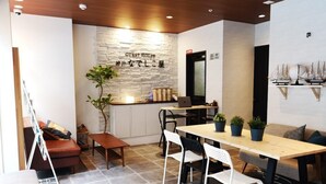 A modern guest house interior with a wooden ceiling, a stone accent wall, a dining area with a wooden table and chairs, a sofa, and a small plant. - Guest House Kobe Nadeshikoya - Hostel (Kobe)
