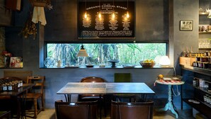 A cozy restaurant interior with a wooden table and chairs, a window with a view of greenery, and a menu board above the window. - Atelier Café bar Seihei (Nakijin)