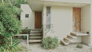 A modern house with a white exterior, a wooden door, a small window, and a set of concrete steps leading to a porch. - Atelier Café bar Seihei (Nakijin)