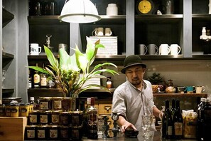A chef in a kitchen with shelves stocked with jars, bottles, and kitchenware. - Atelier Café bar Seihei (Nakijin)