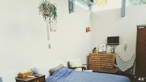 A bedroom with a bed, bedside table, hanging plant, and a desk with a chair. - Atelier Café bar Seihei (Nakijin)