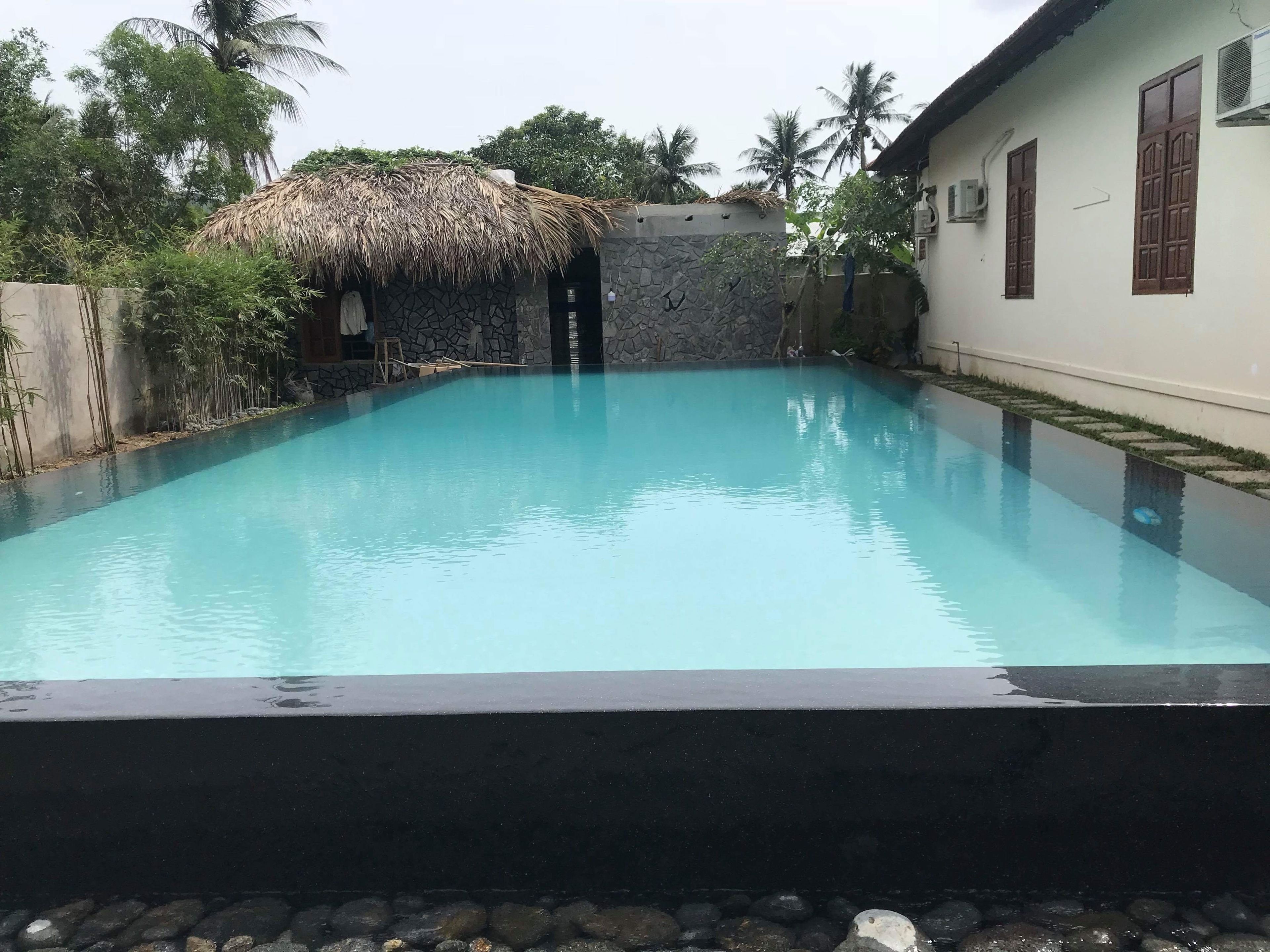 En swimmingpool med en stenvæg og en overdækning med stråtæppe.