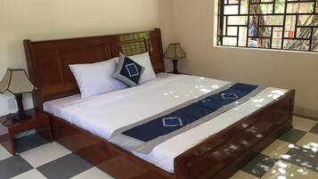 Una cama bien hecha con suelo a cuadros, un cabecero de madera y una ventana con vistas a árboles.