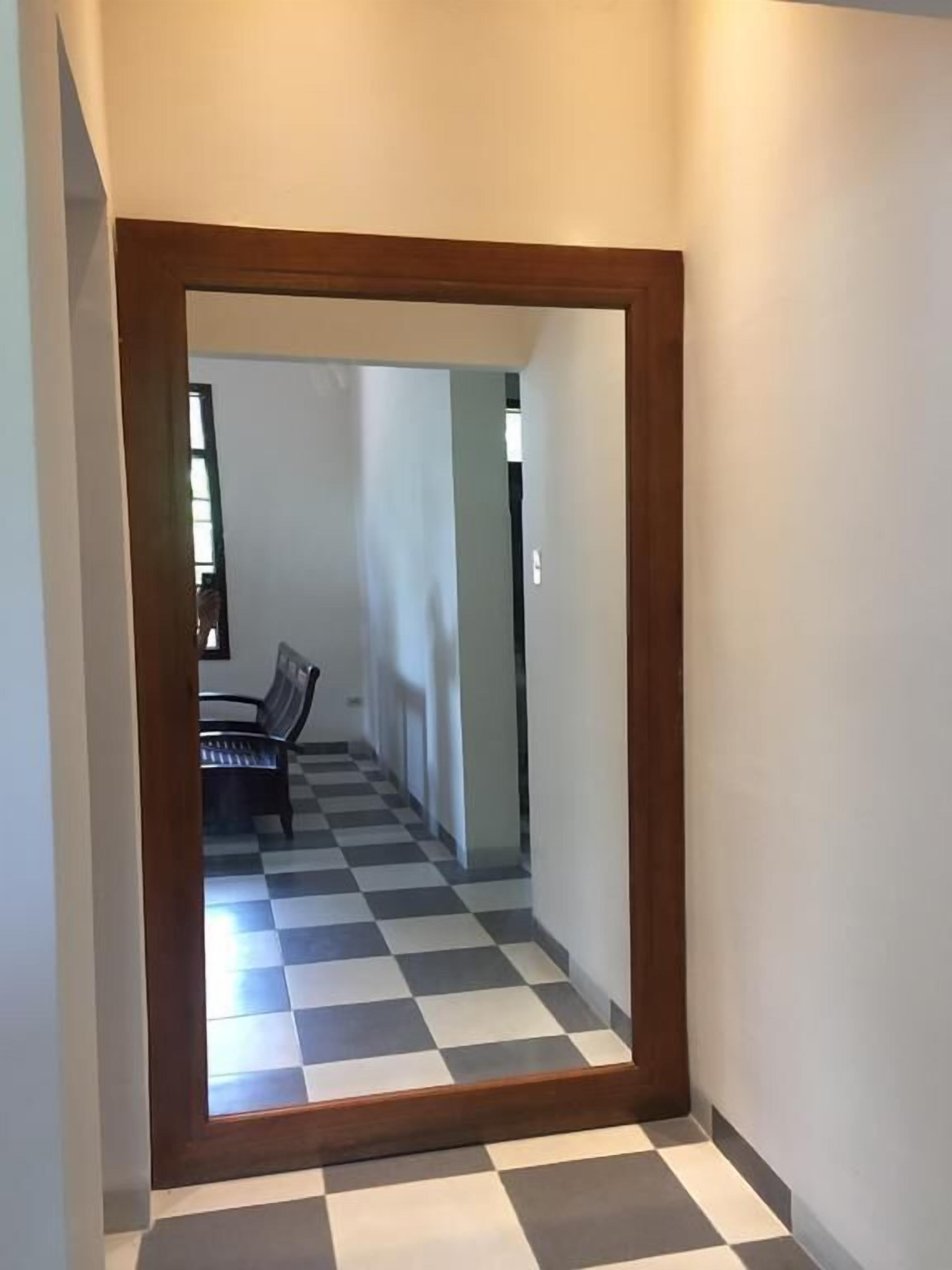 A hallway with a checkered floor and a wooden-framed mirror.
