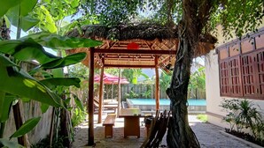 Un espacio de estar al aire libre cubierto con una pérgola de madera, un banco y una mesa.