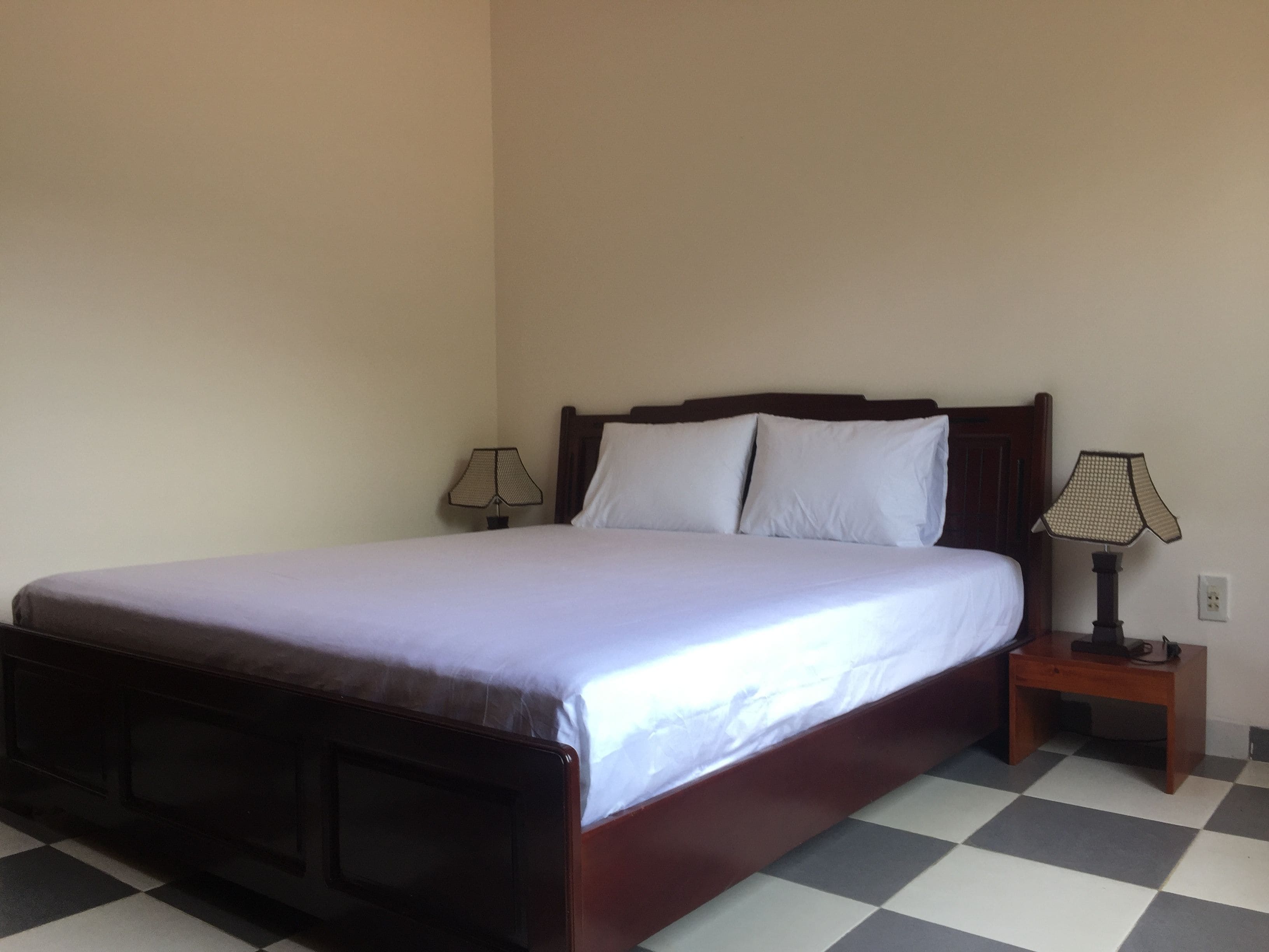 A standard hotel room with a single bed, two bedside tables, and a checkered floor.