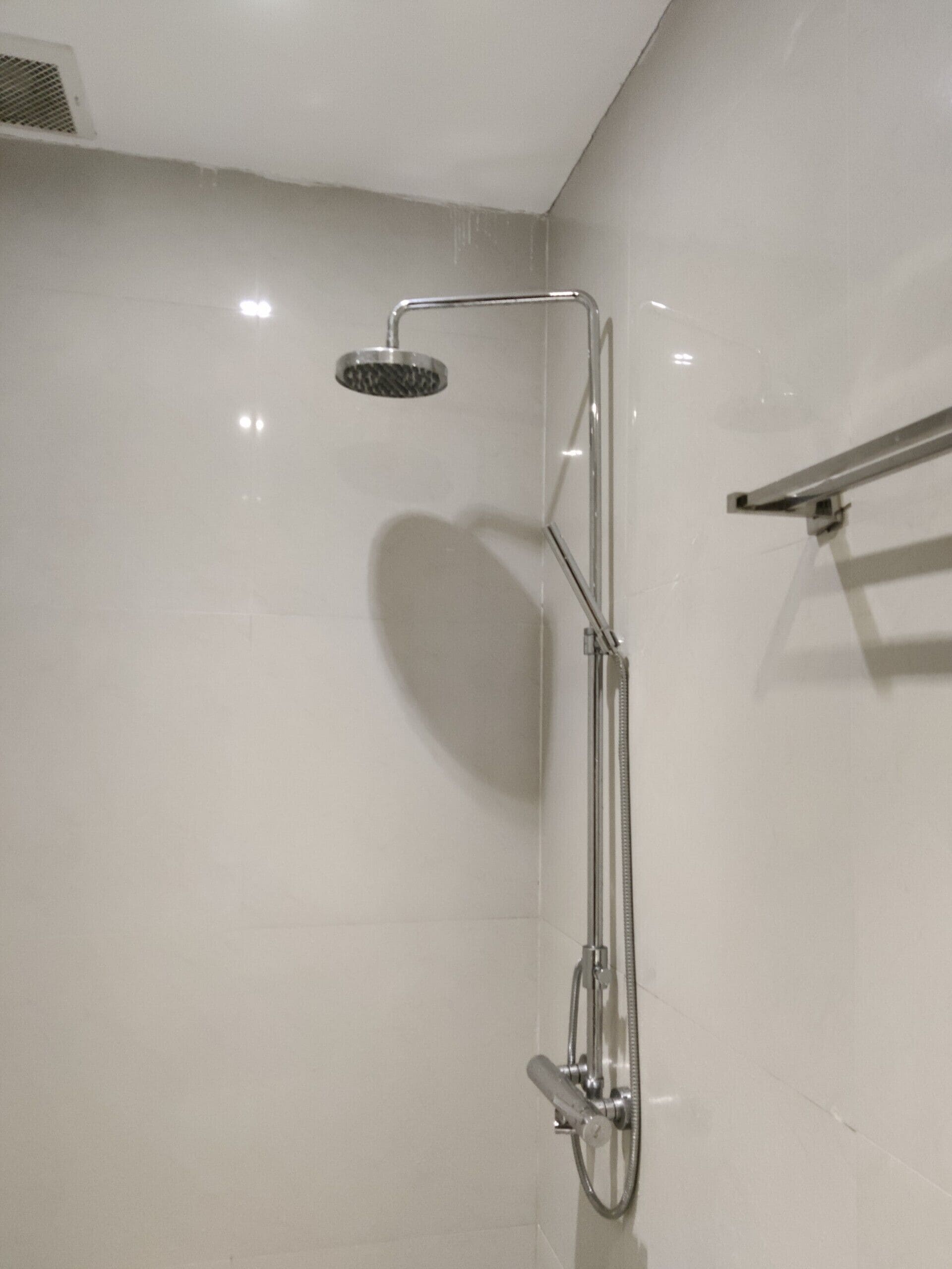 A modern shower with a handheld showerhead and a vertical rain showerhead, mounted on a wall with a chrome finish.