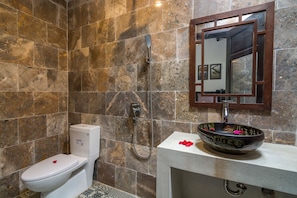 A bathroom with a marble wall, a white toilet, a black vessel sink, and a mirror with a wooden frame.