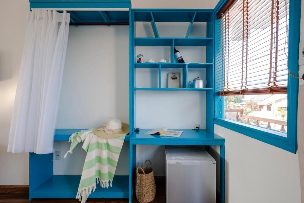 A room with a blue shelf unit, a white curtain, a straw hat, a striped towel, a small basket, and a white appliance.