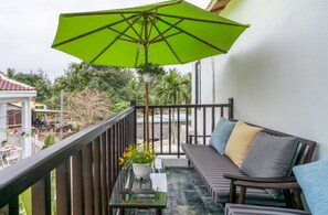 A balcony with a green umbrella, a sofa with cushions, and a table with a potted plant. - An Bang Gate Away (Da Nang)