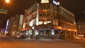 Een hotel met meerdere verdiepingen, een opvallend neonreclamebord, diverse balkons en een café op de begane grond.