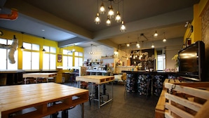 Een restaurantinterieur met houten tafels, hangende lampen en een bakstenen muur.