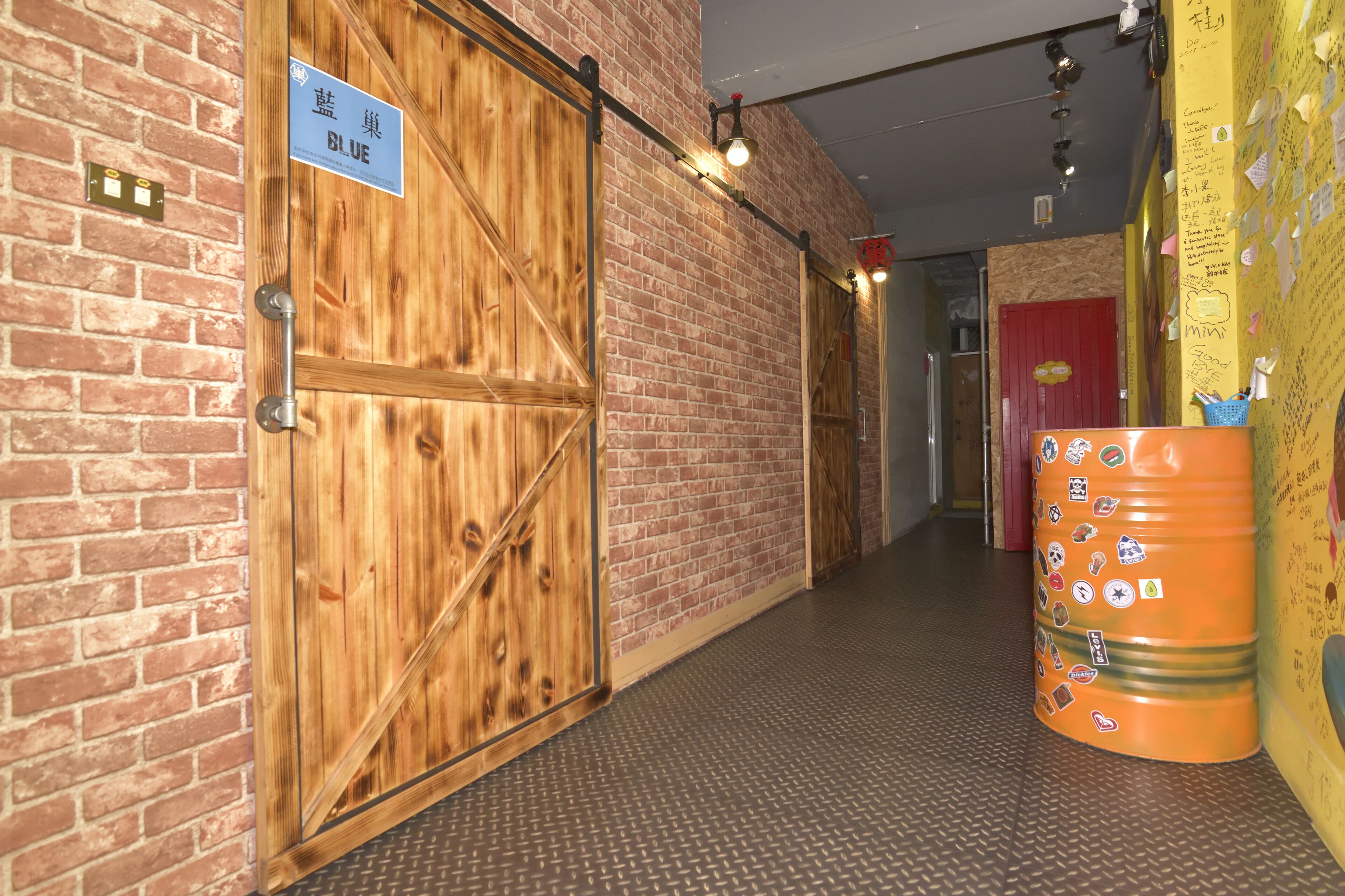 A hallway with a wooden door labeled "BLUE" and a metal handle. There is a textured floor and a large orange barrel with stickers.