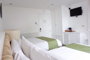 Habitación de hotel con dos camas, un televisor montado en la pared y un escritorio pequeño con cafetera.