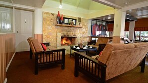 Un salón acogedor con chimenea de piedra, muebles de madera y vistas al exterior a través de amplios ventanales.