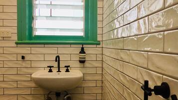 A bathroom with a white sink, green-framed window, and tiled walls.
