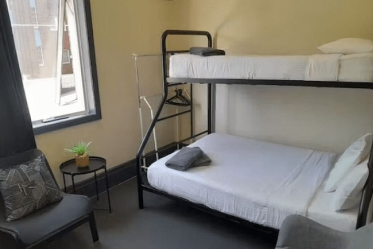 Une chambre avec un lit superposé, une petite table et une chaise, une fenêtre et une plante.