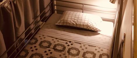 A single bed with a metal frame, a patterned bedspread, and a pillow.