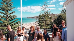A group of people gathered on a balcony overlooking a beach with a clear sky. - Coogee Beach House - Hostel (Coogee)