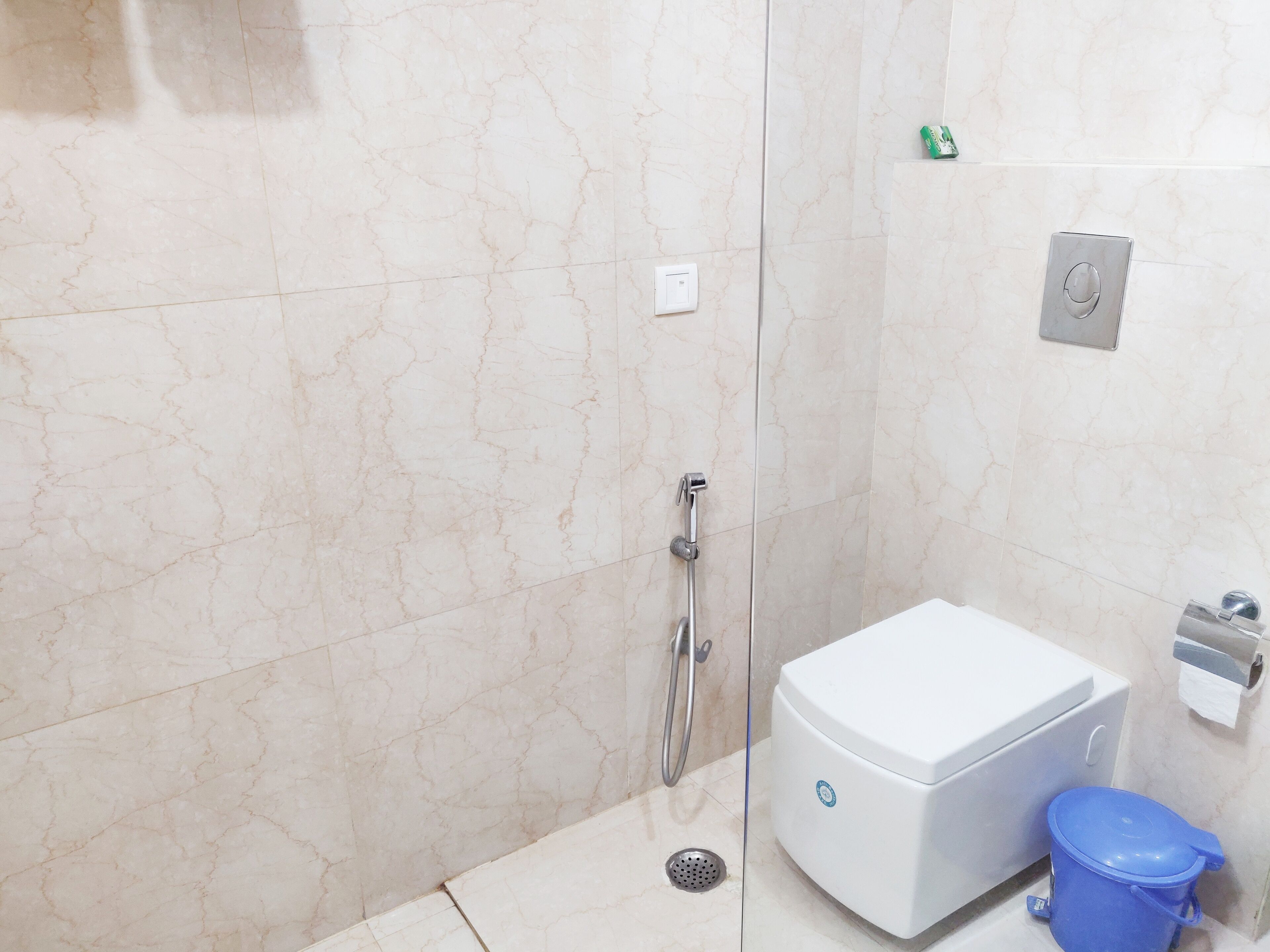 A bathroom with a shower, toilet, and a blue trash bin.