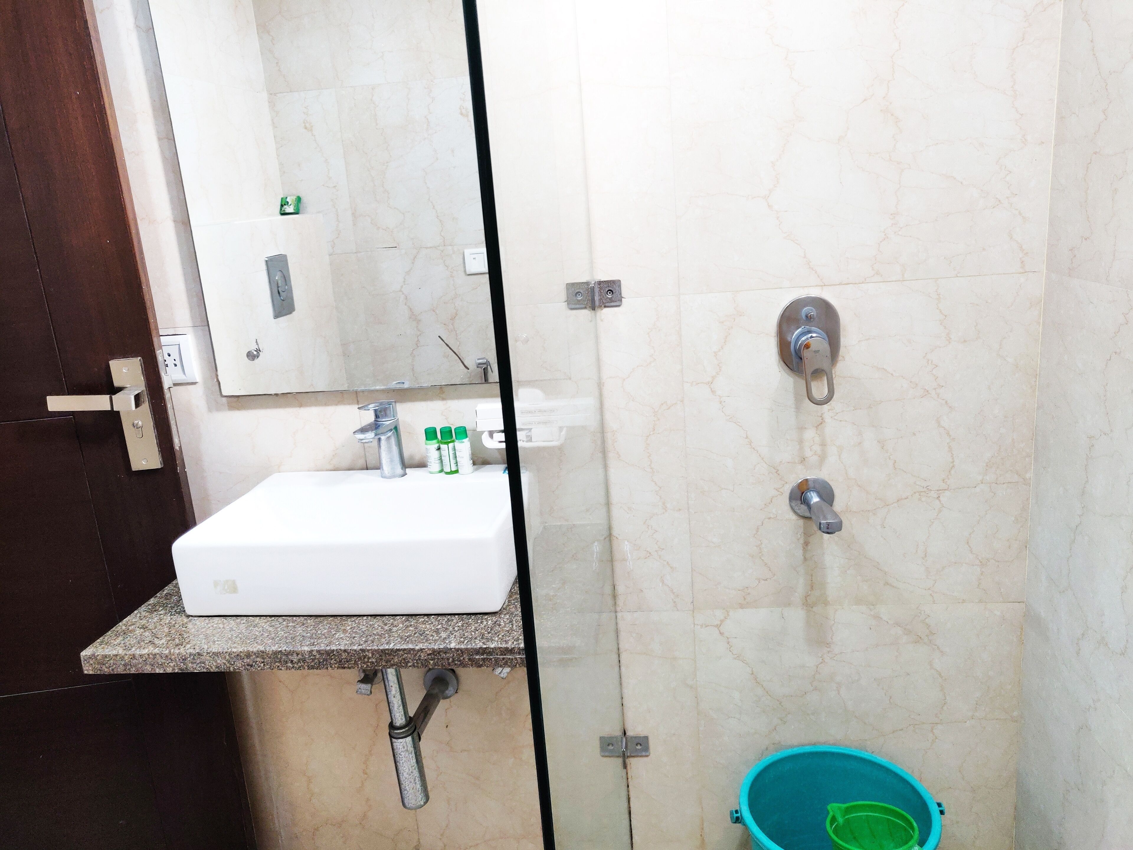 Casa de banho com lavatório branco, espelho, chuveiro com chuveiro de mão e um balde verde.