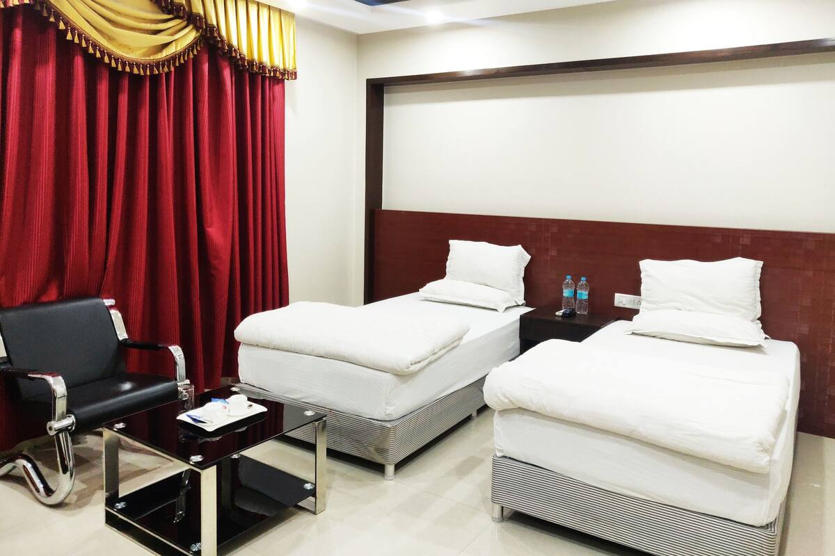 A hotel room with two single beds, a desk, a chair, a red curtain, and a large window.
