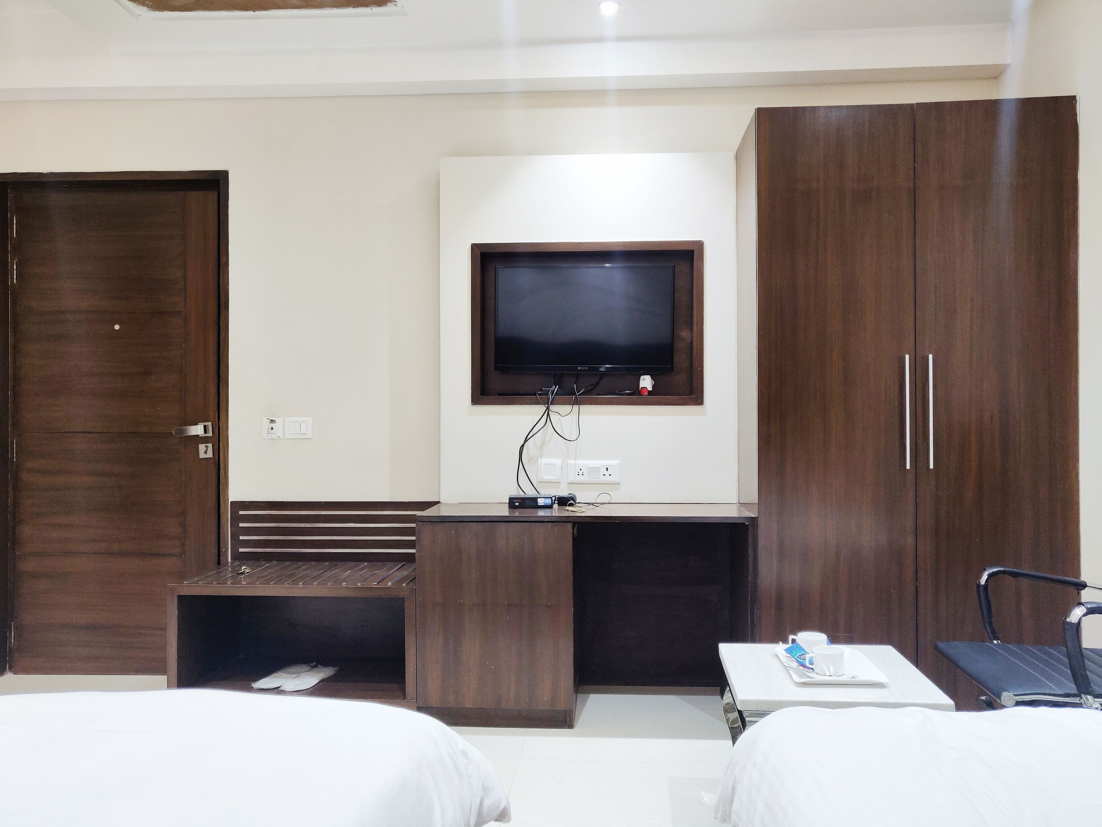 Quarto de hotel com cama, escrivaninha, televisão e guarda-roupa.