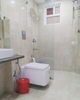 Un baño con inodoro, lavamanos, ducha y un cubo rojo.