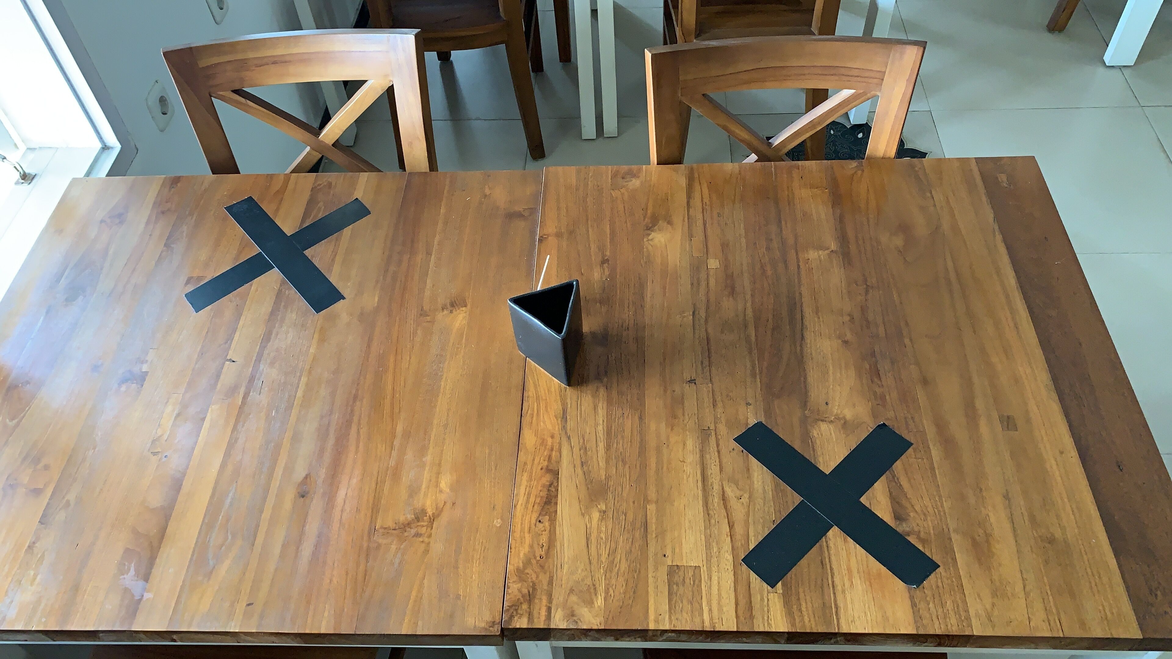 A wooden dining table with a black X-shaped object on each end.